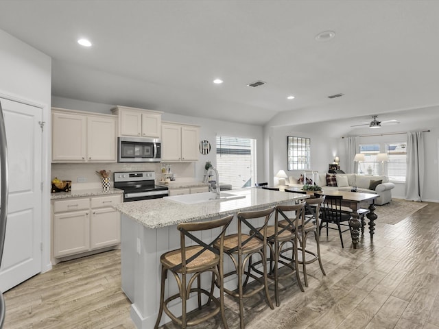 kitchen featuring sink, stainless steel appliances, light stone countertops, white cabinets, and a center island with sink