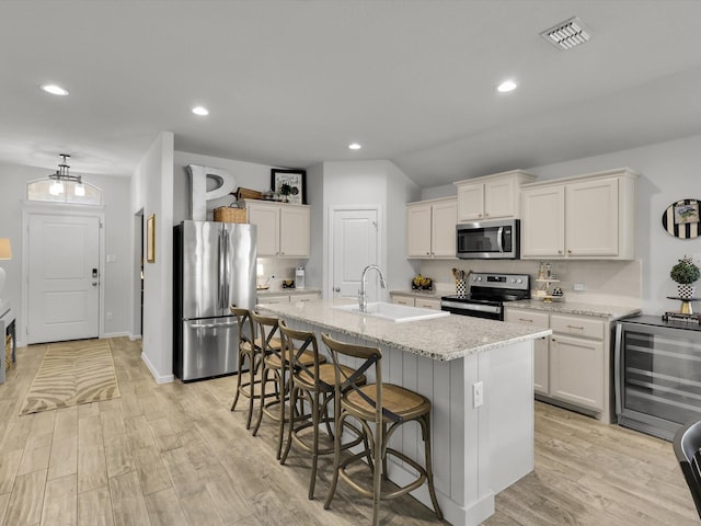 kitchen with white cabinetry, sink, beverage cooler, stainless steel appliances, and a center island with sink