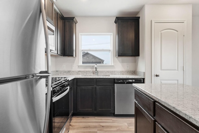 kitchen featuring sink, light hardwood / wood-style flooring, appliances with stainless steel finishes, dark brown cabinets, and light stone countertops