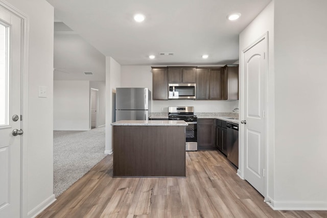 kitchen featuring sink, appliances with stainless steel finishes, dark brown cabinets, a center island, and light colored carpet