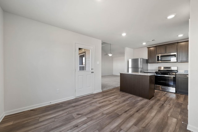 kitchen with dark wood-type flooring, a center island, dark brown cabinets, appliances with stainless steel finishes, and ceiling fan