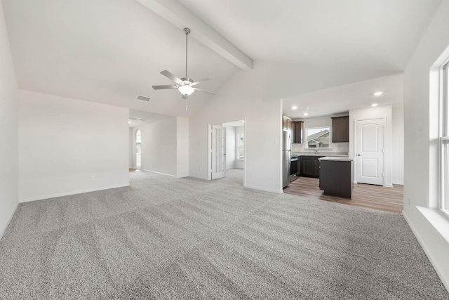 unfurnished living room featuring sink, high vaulted ceiling, ceiling fan, beam ceiling, and carpet