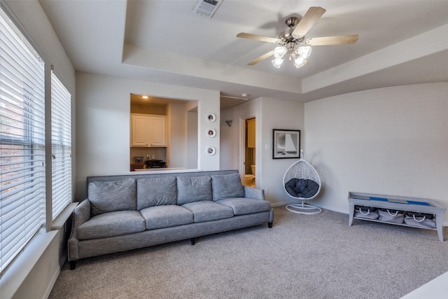 carpeted living room with ceiling fan and a raised ceiling