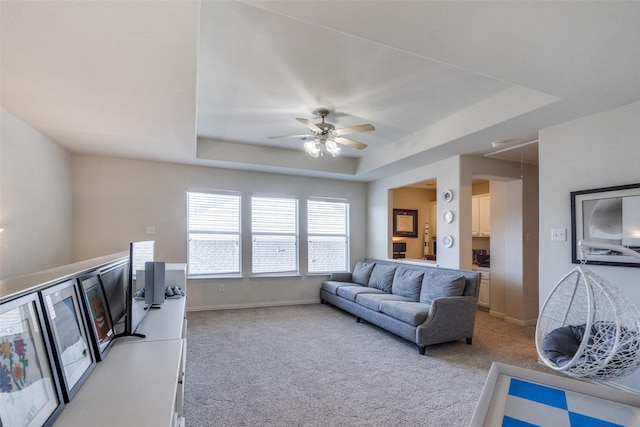 carpeted living room featuring a raised ceiling and ceiling fan