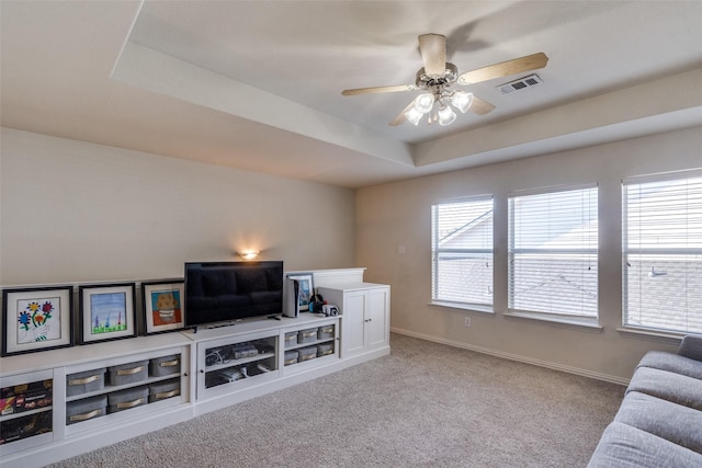 living room featuring light carpet, a raised ceiling, and ceiling fan