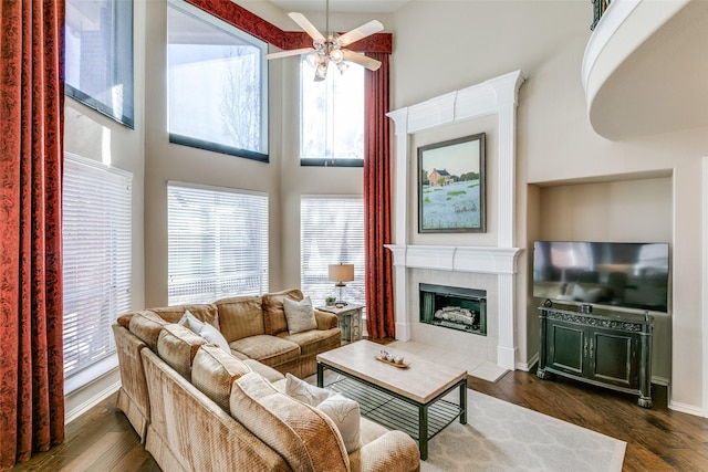 living room with dark wood-type flooring, a tile fireplace, ceiling fan, and a high ceiling