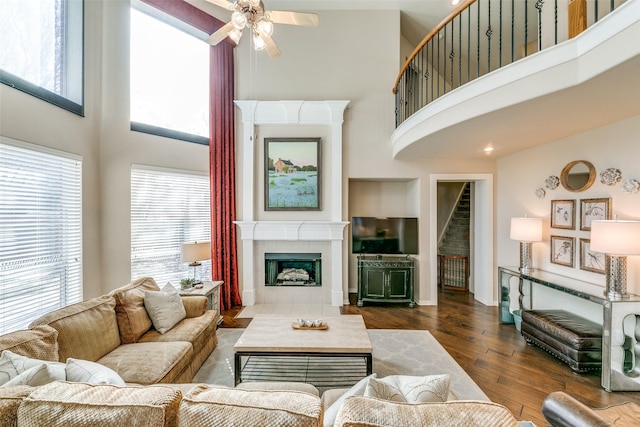 living room with dark hardwood / wood-style flooring, a towering ceiling, a fireplace, and ceiling fan