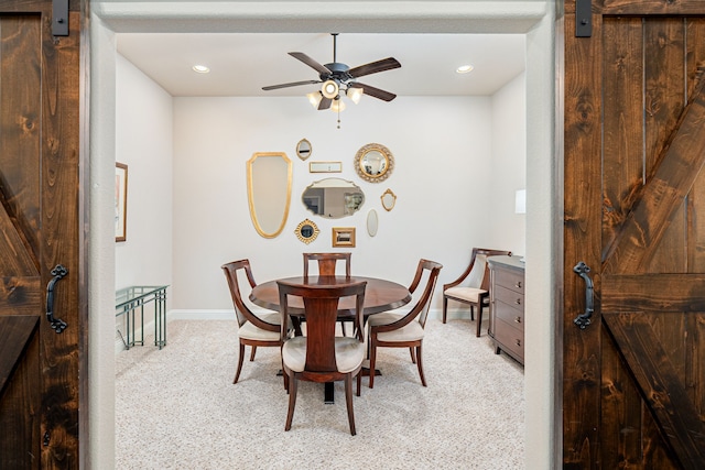 dining room featuring a barn door, light carpet, and ceiling fan