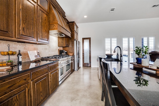 kitchen with crown molding, premium range hood, dark stone counters, and appliances with stainless steel finishes