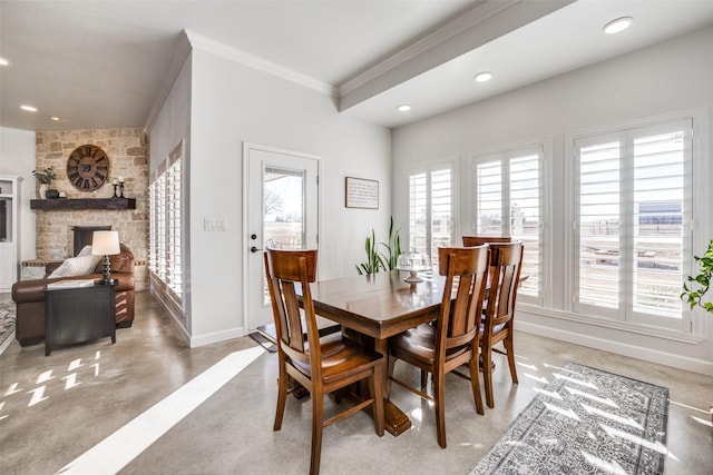 dining space featuring crown molding, concrete flooring, and a stone fireplace