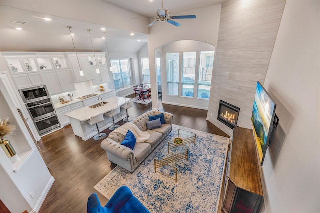 living room featuring lofted ceiling, sink, dark hardwood / wood-style flooring, a tile fireplace, and ceiling fan