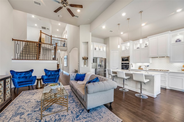 living area featuring visible vents, dark wood-type flooring, stairway, arched walkways, and a ceiling fan