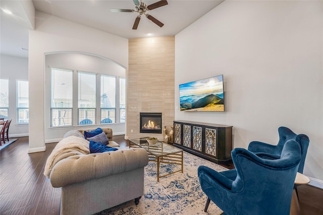 living room featuring dark wood-type flooring, ceiling fan, and a tile fireplace