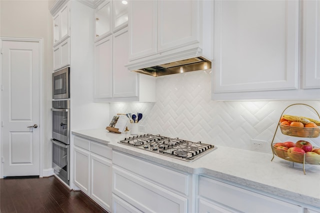 kitchen featuring dark wood-type flooring, appliances with stainless steel finishes, tasteful backsplash, light stone countertops, and white cabinets