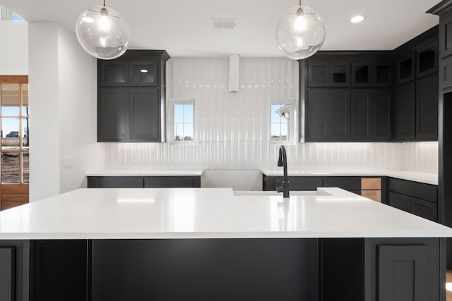 kitchen with pendant lighting, sink, a center island with sink, and backsplash