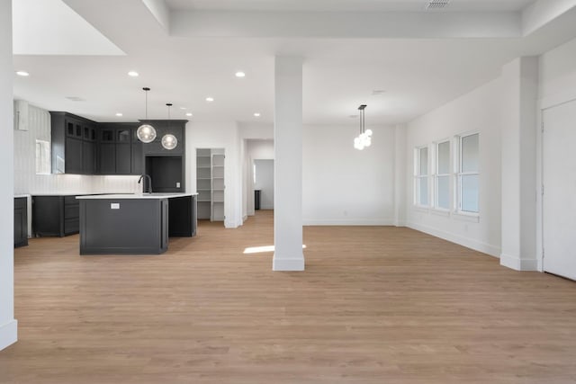 kitchen with sink, hanging light fixtures, a kitchen island with sink, a notable chandelier, and light hardwood / wood-style floors