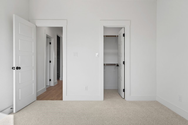 unfurnished bedroom featuring light carpet, a walk in closet, and a closet