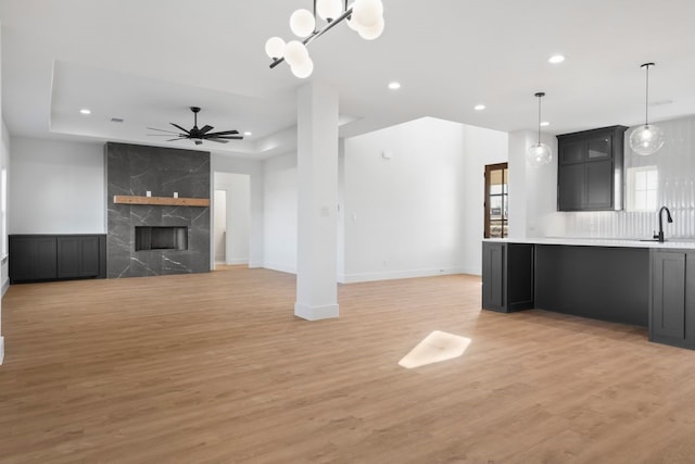 unfurnished living room with sink, a premium fireplace, ceiling fan, a raised ceiling, and light wood-type flooring