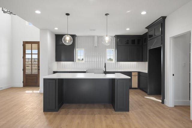 kitchen with tasteful backsplash, pendant lighting, an island with sink, and light wood-type flooring