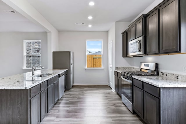 kitchen with appliances with stainless steel finishes, wood-type flooring, sink, light stone counters, and dark brown cabinetry