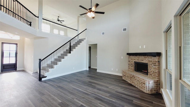 unfurnished living room with ceiling fan, dark hardwood / wood-style floors, a brick fireplace, and a high ceiling