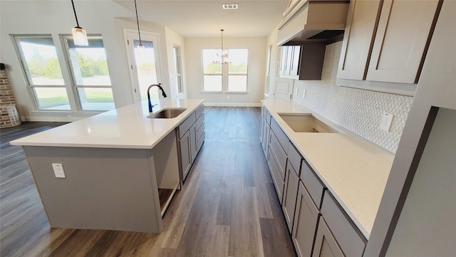 kitchen featuring decorative light fixtures, sink, decorative backsplash, and a center island with sink