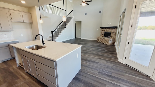 kitchen with sink, decorative light fixtures, a center island with sink, dark hardwood / wood-style flooring, and a fireplace