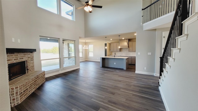 unfurnished living room with a high ceiling, dark hardwood / wood-style floors, ceiling fan with notable chandelier, and a fireplace