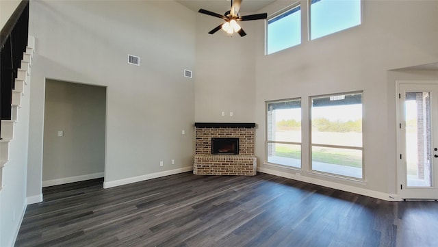 unfurnished living room with dark hardwood / wood-style flooring, a fireplace, ceiling fan, and a high ceiling