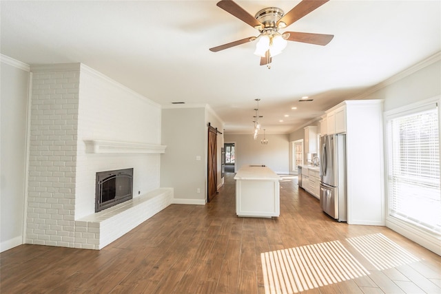 kitchen with white cabinetry, plenty of natural light, stainless steel fridge, pendant lighting, and a kitchen island with sink