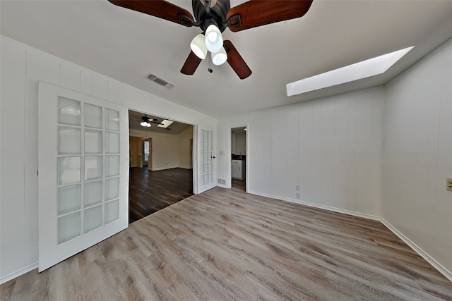 empty room with ceiling fan, a skylight, and hardwood / wood-style floors