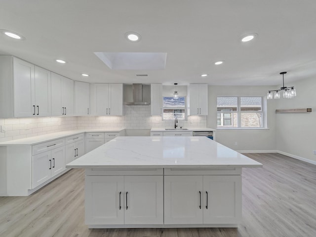 kitchen featuring white cabinetry, wall chimney exhaust hood, decorative light fixtures, and sink