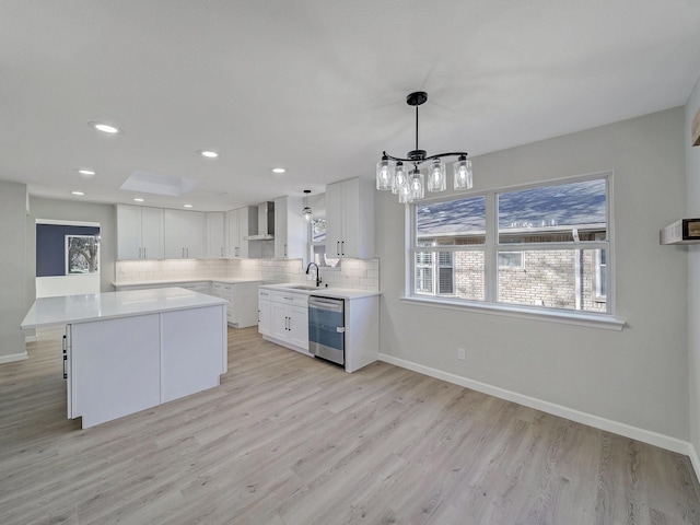 kitchen featuring pendant lighting, wall chimney range hood, white cabinets, decorative backsplash, and stainless steel dishwasher