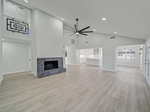 unfurnished living room with high vaulted ceiling, ceiling fan with notable chandelier, a high end fireplace, and light hardwood / wood-style floors