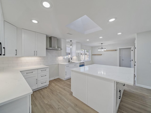 kitchen with pendant lighting, wall chimney exhaust hood, a center island, and white cabinets