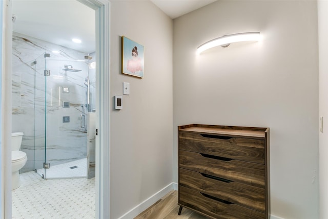 bathroom featuring toilet, a shower with shower door, and hardwood / wood-style floors