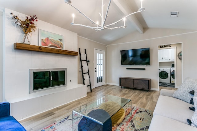 living room featuring a tile fireplace, vaulted ceiling with beams, a chandelier, independent washer and dryer, and light hardwood / wood-style flooring