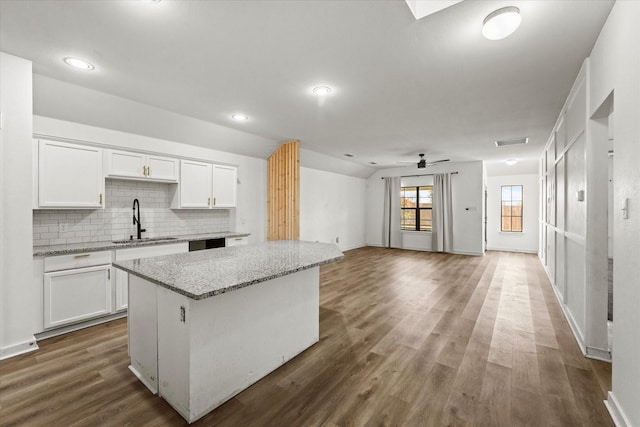 kitchen featuring sink, light stone counters, a center island, decorative backsplash, and white cabinets