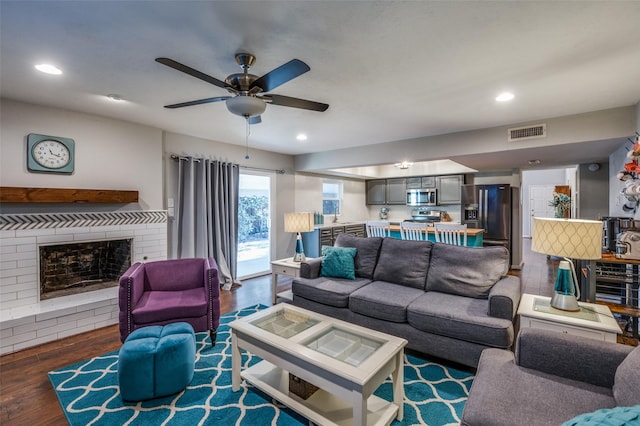 living room featuring ceiling fan, a brick fireplace, and dark hardwood / wood-style flooring