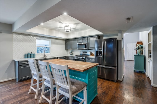 kitchen featuring stainless steel appliances, dark hardwood / wood-style floors, a center island, a tray ceiling, and wood counters