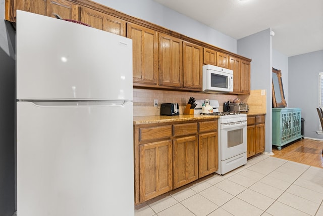 kitchen featuring light tile patterned flooring, white appliances, light stone countertops, and decorative backsplash