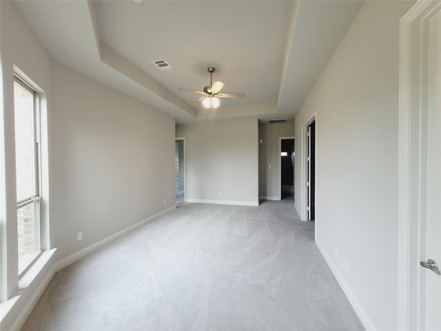 empty room with a raised ceiling, light colored carpet, and ceiling fan