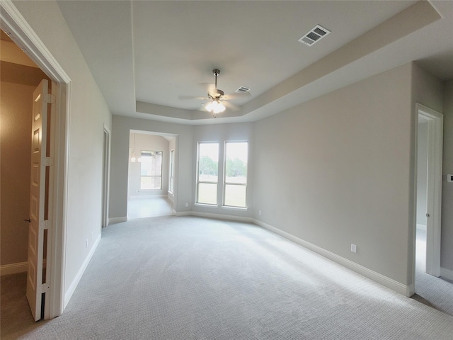 carpeted spare room with a raised ceiling and ceiling fan