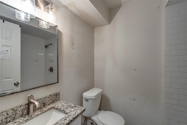 bathroom with vanity, tiled shower, and toilet