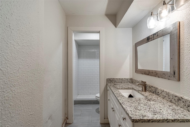 bathroom with tiled shower, vanity, and toilet