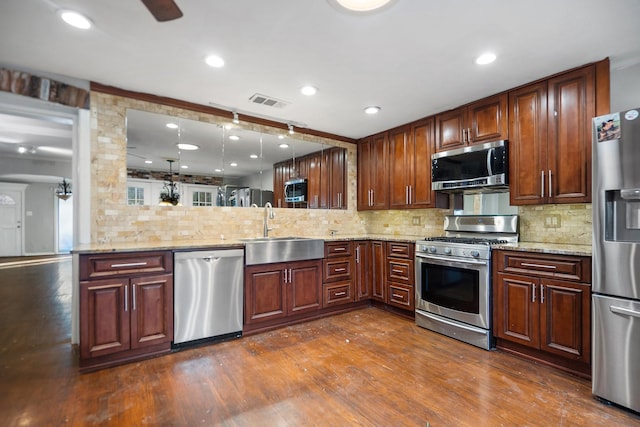 kitchen with dark wood-type flooring, sink, hanging light fixtures, appliances with stainless steel finishes, and kitchen peninsula