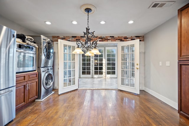 laundry area with french doors, stacked washer / drying machine, dark hardwood / wood-style flooring, and a chandelier