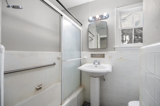 full bathroom with enclosed tub / shower combo, toilet, sink, and tile walls