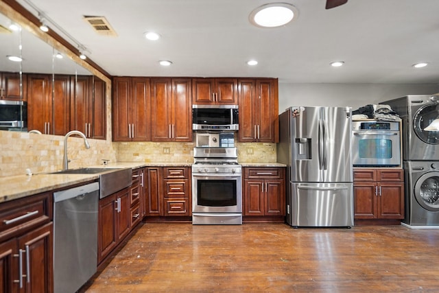 kitchen with sink, appliances with stainless steel finishes, light stone counters, stacked washer / drying machine, and dark hardwood / wood-style flooring