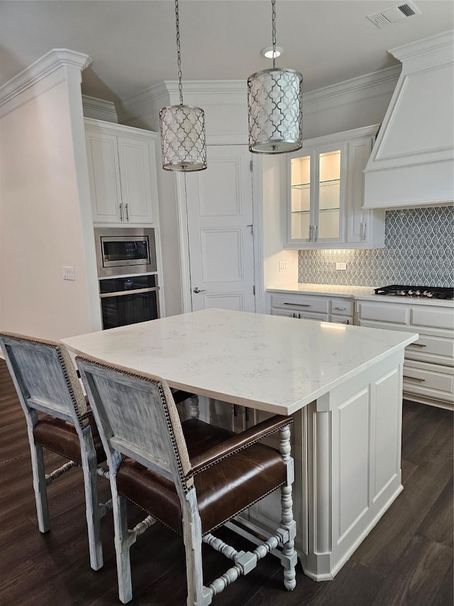 kitchen with custom exhaust hood, hanging light fixtures, stainless steel appliances, decorative backsplash, and white cabinets